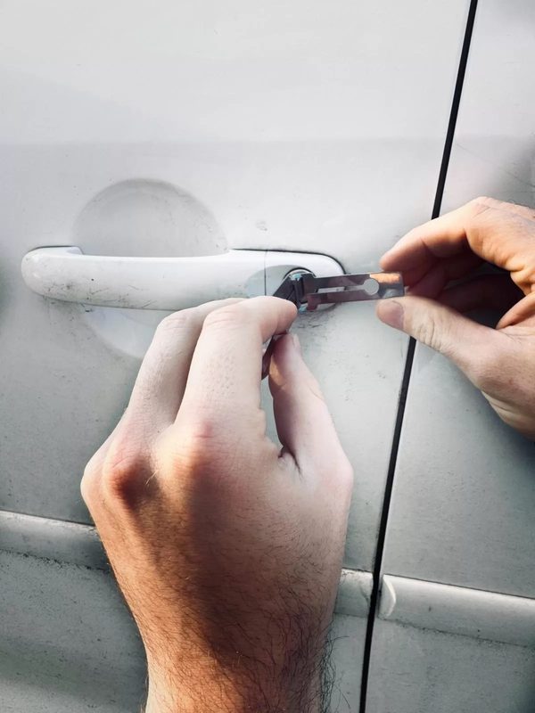 Ruce zámečníka otevírají zámek dveří bílého auta speciálním nástrojem
